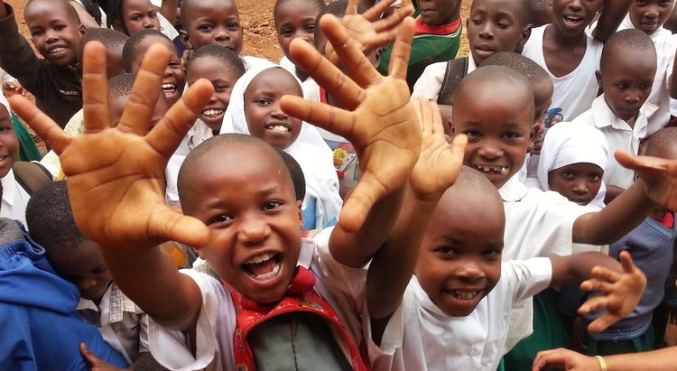 Young students in Kenya are raising their arms and smiling at the camera
